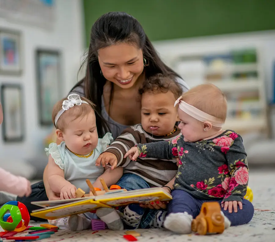 Childcare Worker Reading With Three Infants