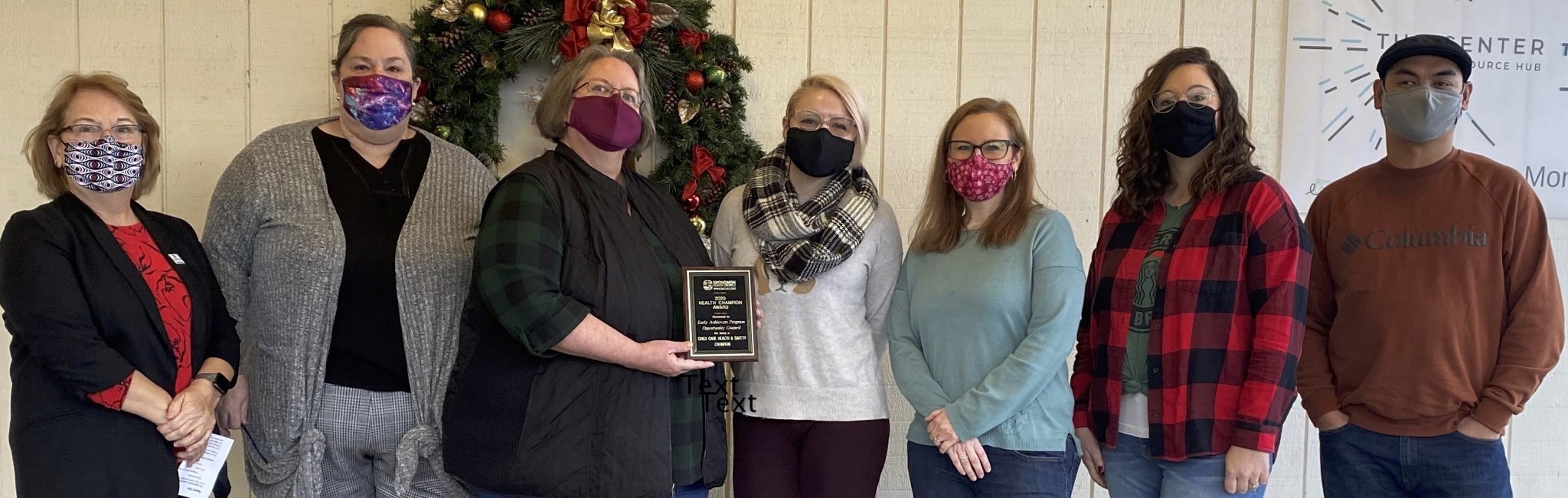 Masked staff from CCA NW WA stand up to receive award, center person holds plaque